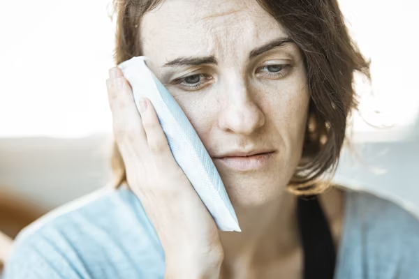 a woman staring into space and holding an icepack to her cheeks due to teeth pain
