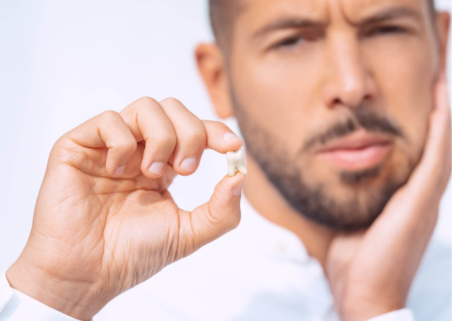 Man holding an extracted tooth and touching his jaw, illustrating common symptoms and discomfort associated with what a cracked tooth feels like.