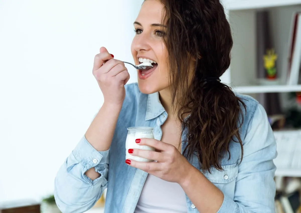 Woman eating soft yogurt with a spoon, an example of what to eat after wisdom teeth removal.